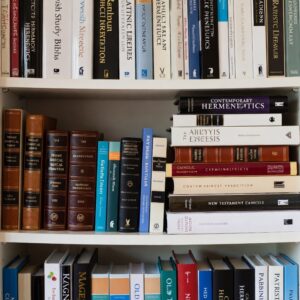 Police plné knih o biblické hermeneutice a výkladu Písma – viditelné tituly jako „Catholic Interpretation“, „Rabbinic Literature“, „Contemporary Hermeneutics“, „Patristic Exegesis“ a další, uspořádané v několika řadách na bílých policích.