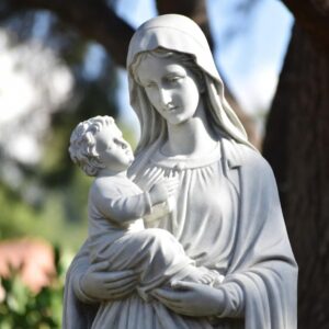 Socha Panny Marie držící malého Ježíše v náručí. Maria se s jemným výrazem sklání k dítěti, které se k ní přimyká a dotýká se jejího roucha. Socha symbolicky připomíná mateřství Panny Marie a její jedinečné místo v dějinách spásy. V křesťanské tradici se právě k Marii věřící obracejí v modlitbě Zdrávas Maria, která vychází z biblických slov anděla Gabriela a Alžběty a prosí Matku Boží o přímluvu u jejího Syna Ježíše Krista. Obrázek tak vizuálně vyjadřuje vztah mezi Marií a Ježíšem, jenž stojí v centru této známé katolické modlitby.