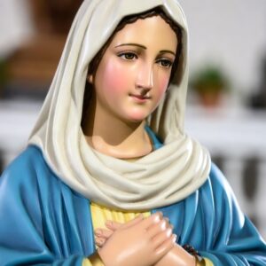 Alternativní text (alt text): Detailní pohled na sochu Panny Marie s jemným a klidným výrazem tváře. Maria má sepjaté ruce položené na hrudi v gestu modlitby a pokory. Je oblečena do modrého pláště a světlého závoje, který symbolizuje její čistotu a oddanost Bohu. Socha připomíná postoj vnitřního soustředění a důvěry, který je vlastní i modlitbě Zdrávas Maria. Tento obraz může inspirovat k osobní modlitbě, ve které se věřící obrací k Bohu a zároveň prosí Pannu Marii, Matku Ježíše Krista, o přímluvu, ochranu a vedení na cestě víry.