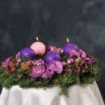 Adventní věnec s fialovými a růžovými svícemi na tmavém pozadí
