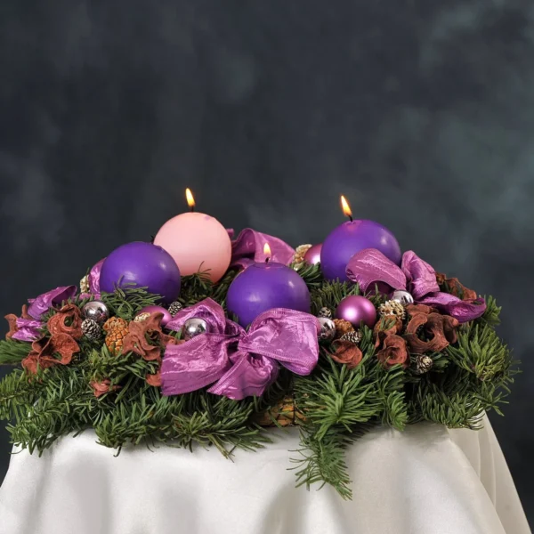 Adventní věnec s fialovými a růžovými svícemi na tmavém pozadí