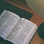 Otevřená moderní Bible položená na tmavé podložce u dřevěného stolu