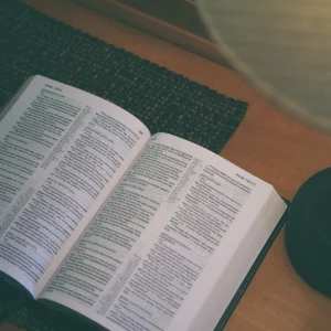 Otevřená moderní Bible položená na tmavé podložce u dřevěného stolu
