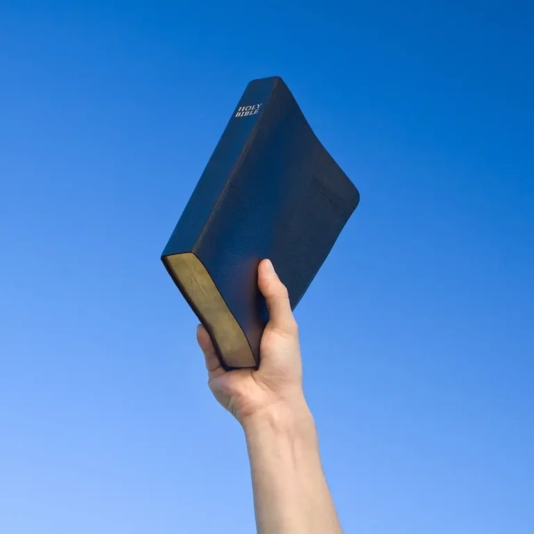 Ruka držící Bibli proti modré obloze