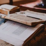 Několik otevřených knih a psací potřeby rozložené na stole