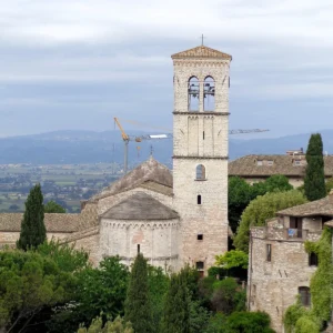 Kamenná bazilika s hranolovou zvonicí nad krajinou Assisi