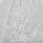 Detail bílé krajkové látky s jemně vyšívanými květinami
