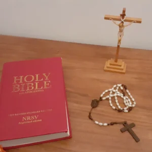 Červená Bible, dřevěný kříž a bílý růženec na stole