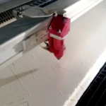 Laserová řezačka vyřezávající geometrické tvary do bílé pěnové desky