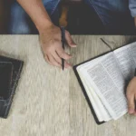 Otevřená Bible na stole a ruce zapisující poznámky