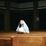 Žena klečí v kostelní lavici a modlí se s růžencem v rukou