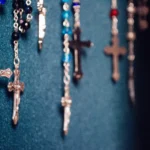 Několik růženců s křížky zavěšených před modrým pozadím