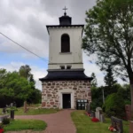 Kamenná kostelní zvonice se hřbitovem pod zataženou oblohou