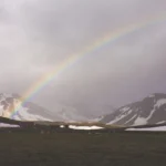 Duha nad tmavou krajinou a zasněženými horami na Islandu