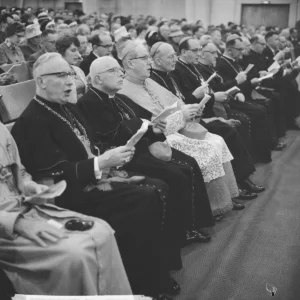 Černobílý záběr duchovních sedících v řadách na církevním shromáždění