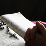 Sepjaté ruce nad otevřenou Biblí s položeným růžencem
