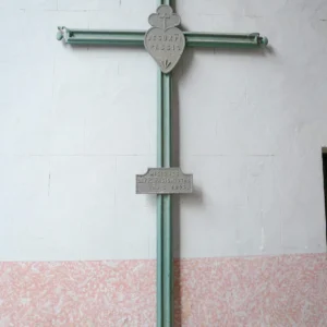 Zelený kovový kříž upevněný na bílé kostelní stěně
