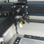 Detail laserové hlavy nad pracovním stolem s měřicími stupnicemi